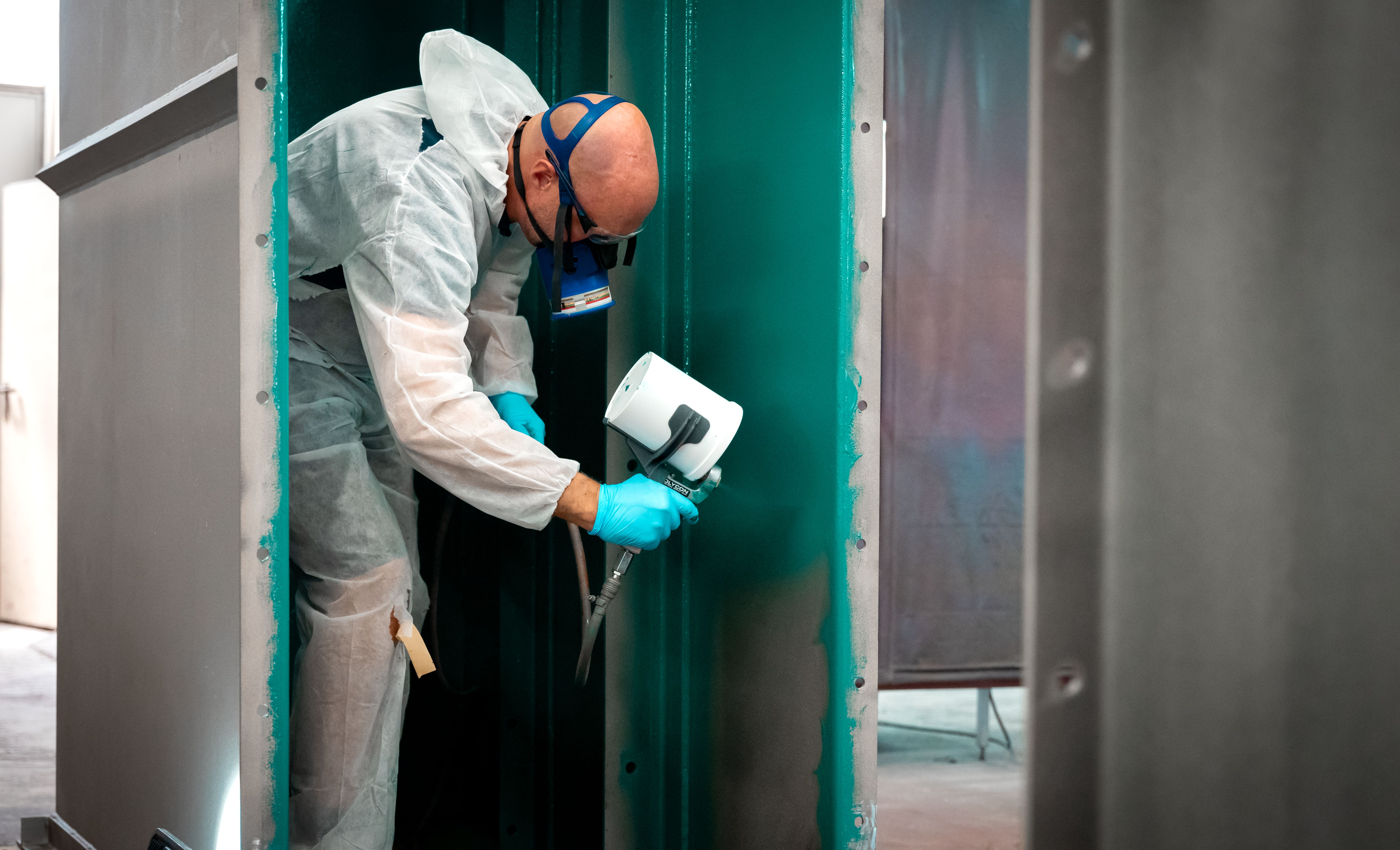 Muž s maskou nastříká zelenou kontrolní vrstvu