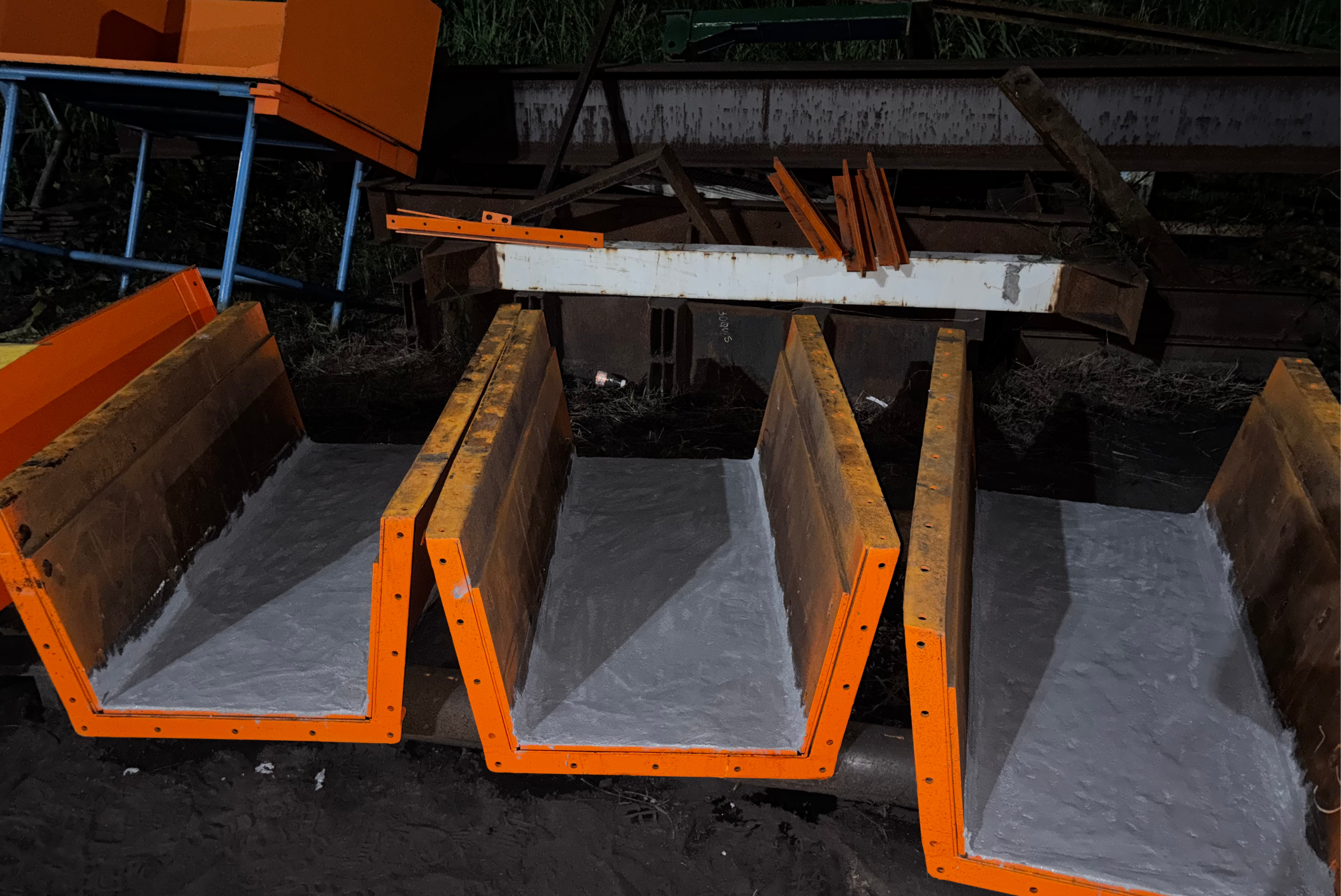 Pohled na řadu několika oranžových kovových žlabů, jejichž vnitřní část je rovnoměrně pokryta šedou ochrannou vrstvou pro odolnost vůči opotřebení.