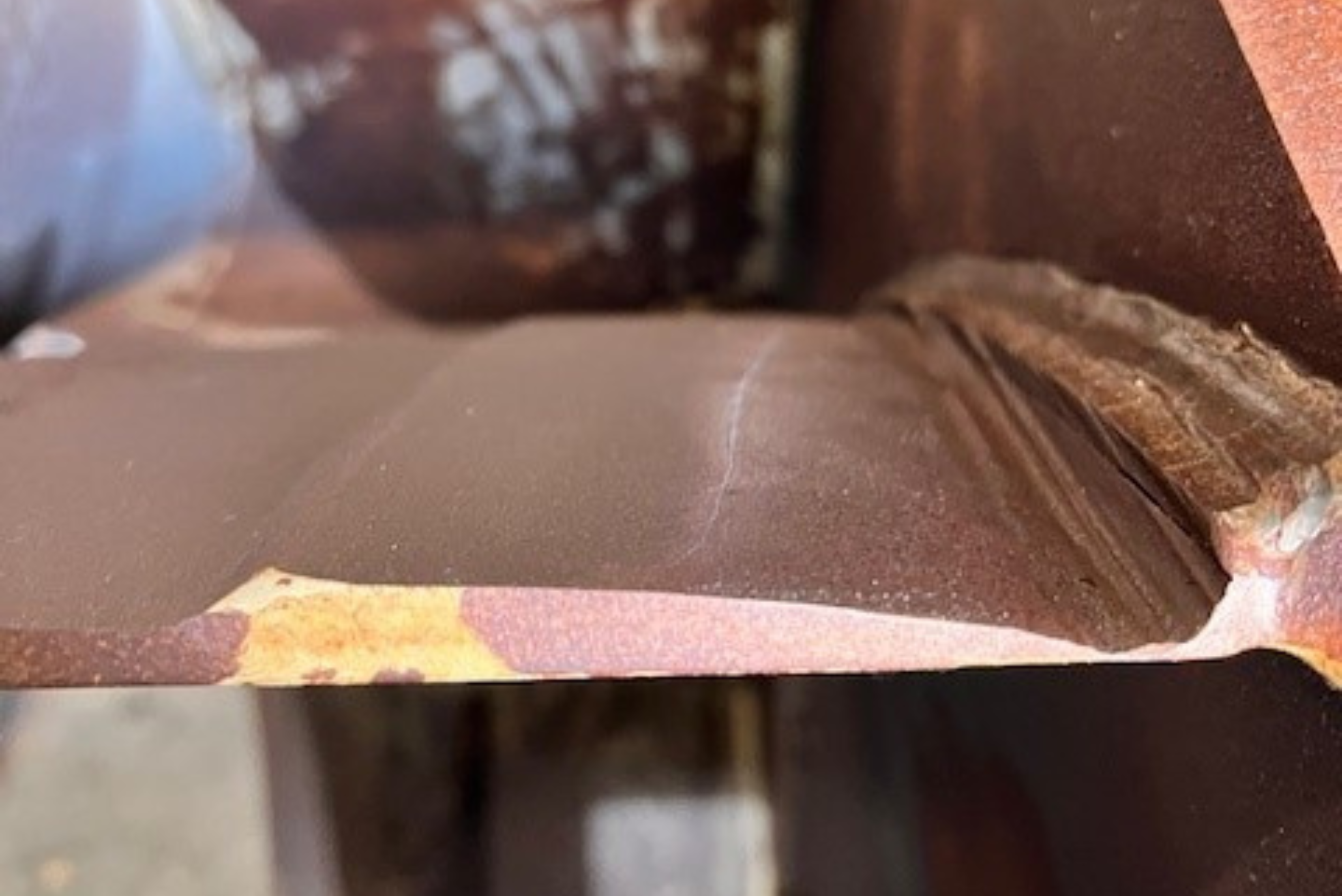 Close-up of a brownish metal component showing its layered structure and a welded seam along the joint.