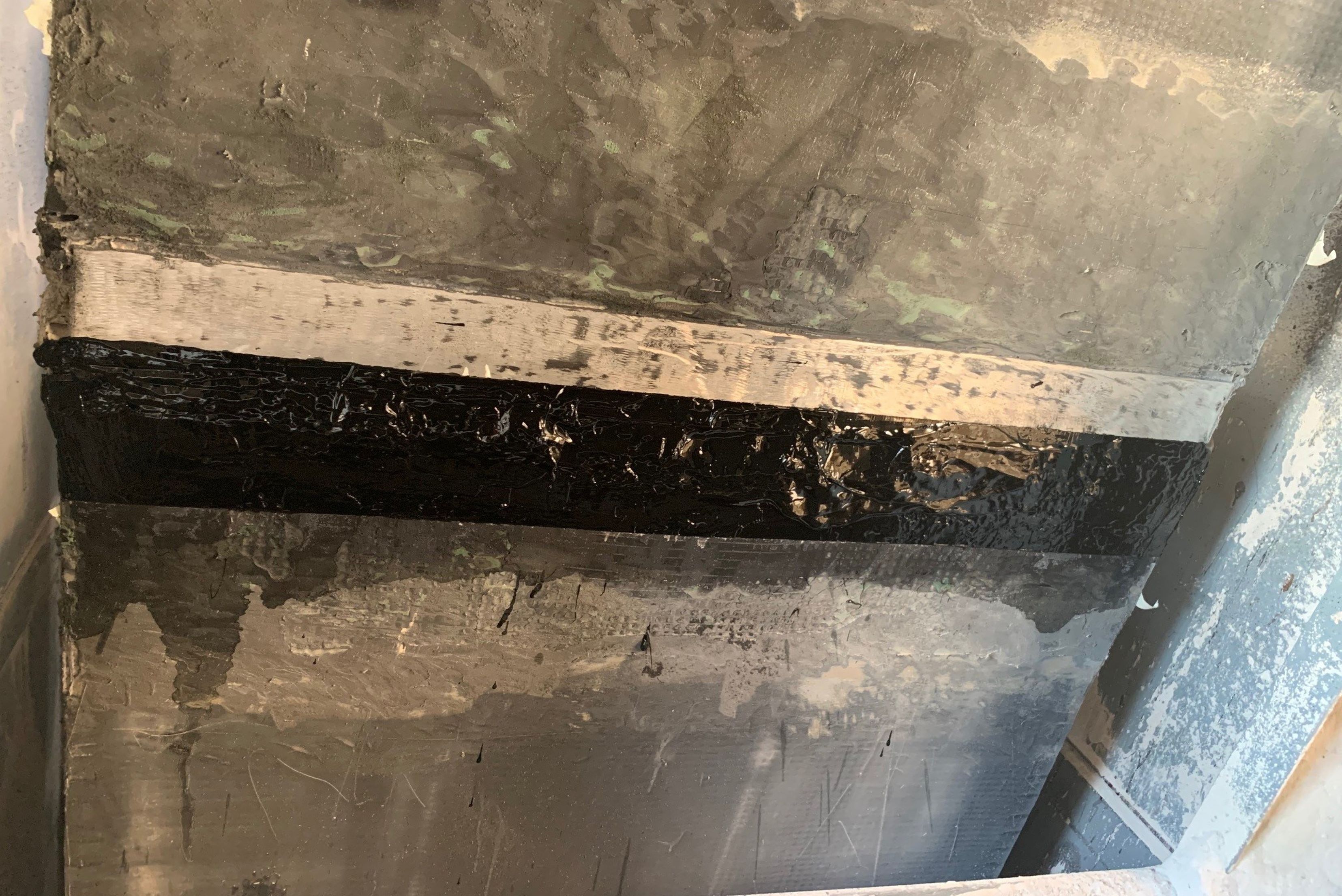 Detailní pohled na opravenou plochu průmyslového obložení s nově aplikovaným černým těsnicím nebo ochranným pruhem v místě spoje.
