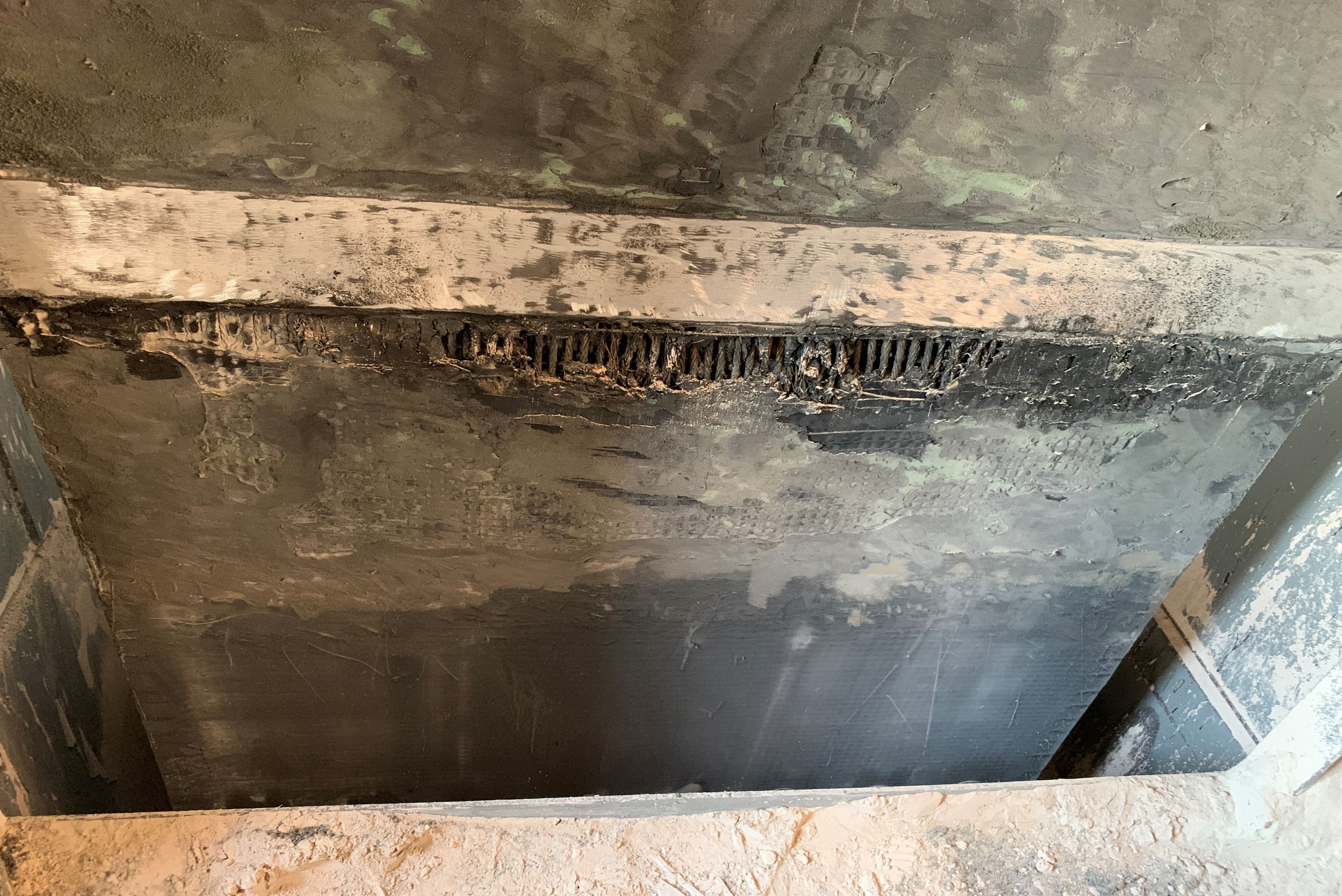 Detailní pohled na poškozený nebo opotřebovaný povrch průmyslového obložení s patrným poškozením struktury v horní části.
