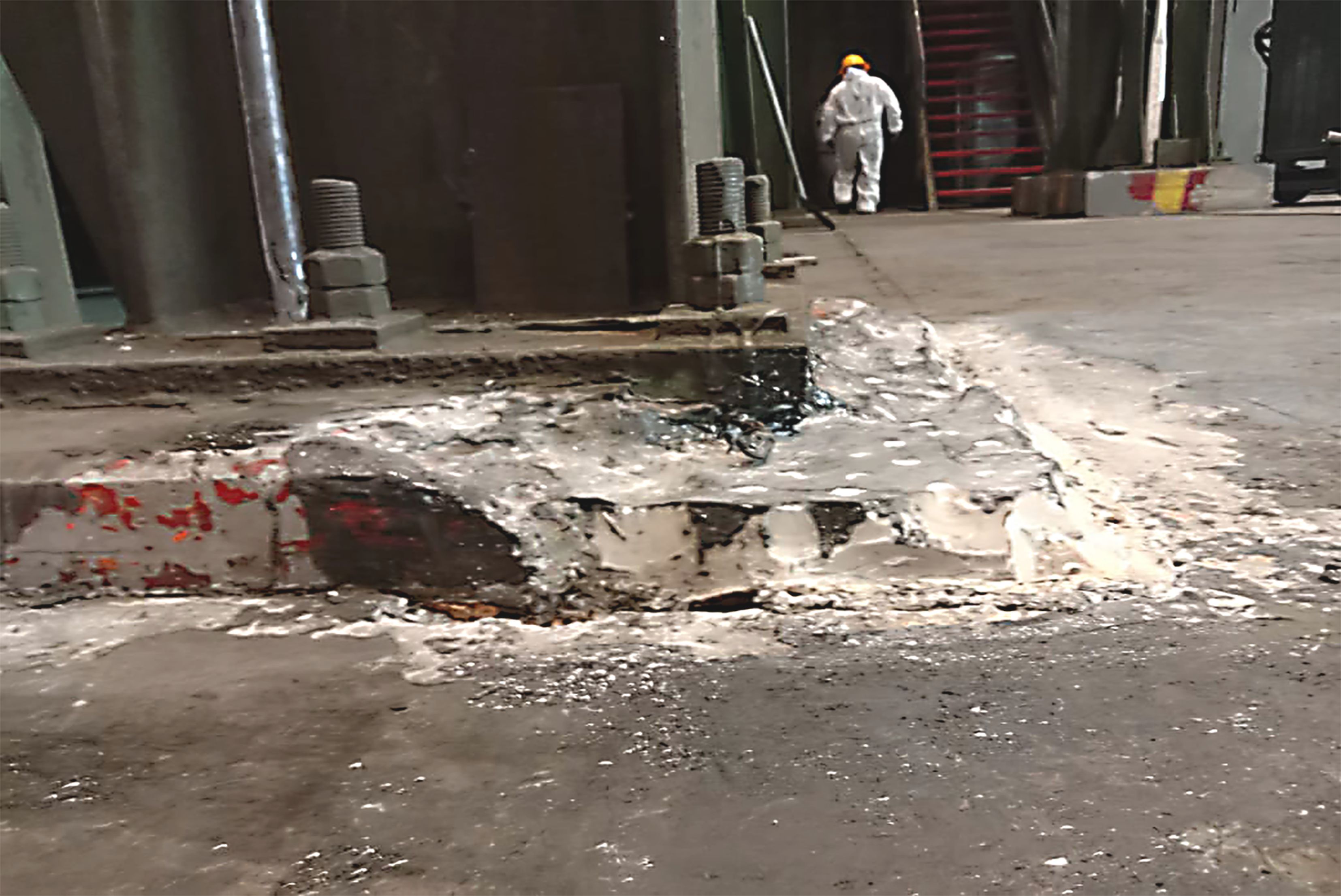 Pohled na poškozenou betonovou základovou desku průmyslového stroje s upevňovacími šrouby, vyžadující opravu a renovaci povrchu.